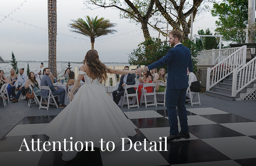 A bride and groom dance on a black-and-white checkered floor outdoors at Heitman House, a stunning waterfront wedding venue. Surrounded by guests, string lights and palm trees set a festive scene. The text reads, Attention to Detail. A bride and groom dance on a black-and-white checkered floor outdoors at Heitman House, a stunning waterfront wedding venue. Surrounded by guests, string lights and palm trees set a festive scene. The text reads, Attention to Detail.