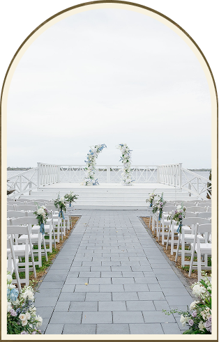 An outdoor waterfront wedding venue with white chairs in rows flanking a stone aisle, leading to a decorated white platform at Heitman House, overlooking the water and adorned with beautiful floral arrangements. An outdoor waterfront wedding venue with white chairs in rows flanking a stone aisle, leading to a decorated white platform at Heitman House, overlooking the water and adorned with beautiful floral arrangements.